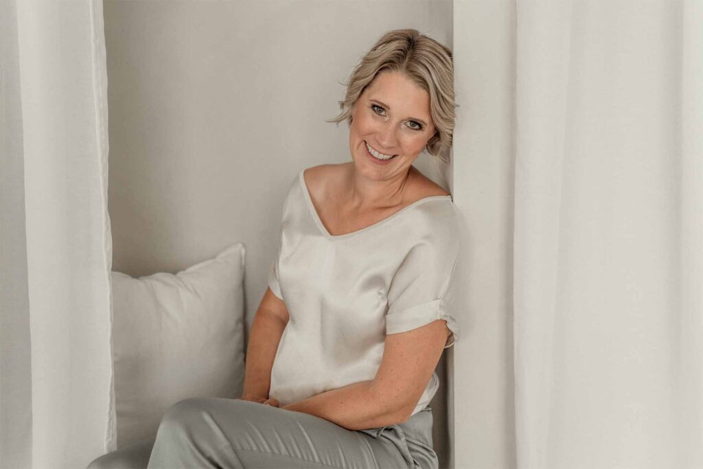 Was ist Achtsamkeit/ Mindfulness?: Julia Jäger sitzend lehnend an einer Wand und lächelt